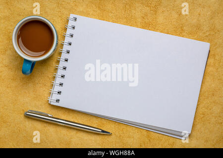 Leere Spirale Art Skizzenbuch gegen Gelb strukturierte Rinde Papier mit einer Tasse Kaffee Stockfoto