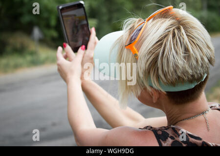 Nach blonde Frau macht selfie auf dem Smartphone auf einem Hintergrund von einem Feld mit Sonnenblumen, selektiver Fokus Stockfoto
