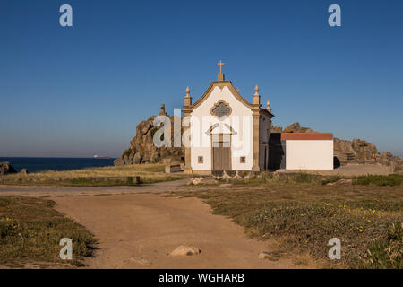 Kleine weiße Kapelle im traditionellen portugiesischen Stil an der Küste des Atlantik, neben einem Felsen. Strahlend blauen Himmel. Porto, Portugal. Stockfoto