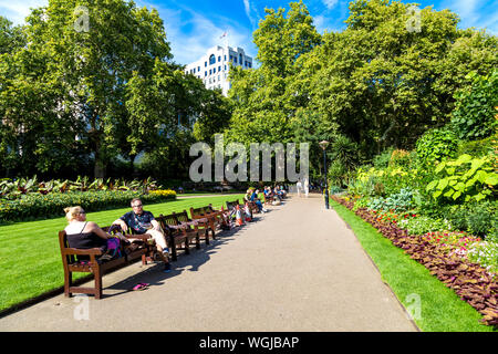 Leute sitzen auf Bänken im Sommer am Victoria Embankment Gardens, London, UK Stockfoto