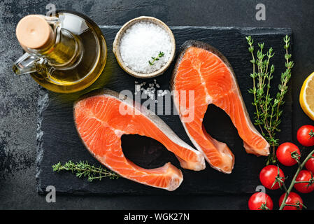 Lachs Steaks und Gewürze zum Kochen auf schwarzem Schiefer Hintergrund, Ansicht von oben. Gesunde Lebensmittel, die reich an Omega-3-Fettsäuren. Stockfoto