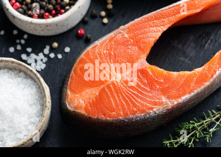 Roher Lachs Steak und Gewürzen auf schwarzem Schiefer Hintergrund bereit zum Kochen Stockfoto