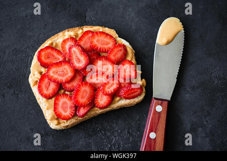 Peanut butter Toast mit frischen Erdbeeren auf schwarzem Hintergrund. Ansicht von oben. Gesündere PB Jelly Sandwich Stockfoto