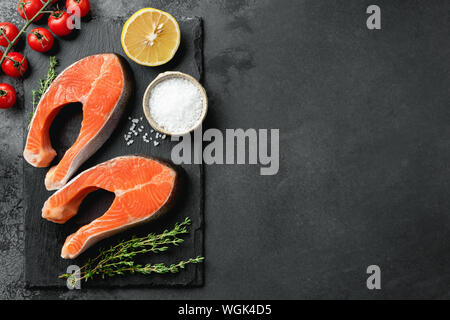 Rohen ungekochten Lachs Steaks und Gewürzen auf schwarzem Schiefer Hintergrund. Ansicht von oben, kopieren Raum Stockfoto