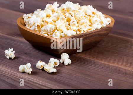 Herzförmige Popcorn in eine hölzerne Schüssel und einer Fernbedienung auf einem Holztisch Stockfoto