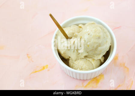 Gelbe vegan selbstgemachte Banane und Mango milchfrei gelato Speiseeis in eine Porzellanschale mit einem Löffel, rosa Hintergrund. Platz kopieren, selektiven Fokus. Stockfoto