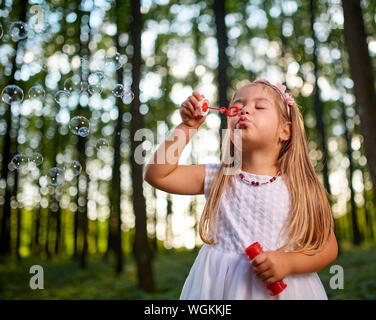 Kleine Mädchen bläst Seifenblasen im Wald Stockfoto