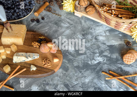 Stillleben mit verschiedenen Sorten von Käse auf Holz- fach, Nüsse, Brot Sticks, Trauben, Rosinen, Wein Korkenzieher Stockfoto