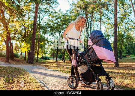 Junge Mutter Walking im Sommer Park mit Kinderwagen. Happy sorgende Frau verbringt Zeit mit Ihrem Kind draußen bei Sonnenuntergang Stockfoto