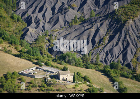 LUFTAUFNAHME. Die Saint-Pons-Kapelle aus dem 12. Jahrhundert von La Robine-sur-Galabre mit einer Landschaft aus Badlands (schwarzem Mergelgrün) im Hintergrund. Frankreich. Stockfoto