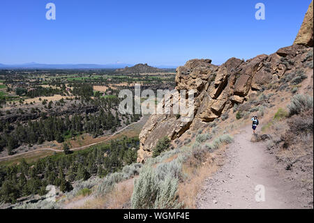 Frau Wanderungen und Fotografien Elend Ridge Trail in Smith Rock State Park in der Nähe von Terrebonne, Oregon am wolkenlosen Sommertag. Stockfoto