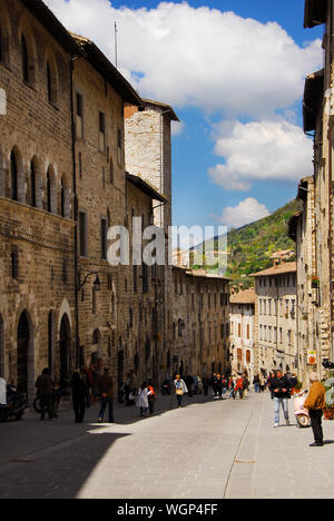 Touristen zu Fuß entlang der Via dei Consoli (Straße der Konsuln), der wichtigsten Einkaufsstraße in der mittelalterlichen Altstadt von Gubbio Stockfoto