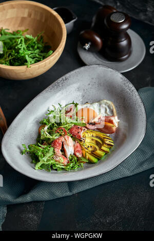 Salat mit Krabben und Avocado auf einem dunklen Hintergrund. Rucola Salat, gewürzt mit Soße auf Weißwein mit Krabben Fleisch und gegrilltem Avocado in sanften fo Stockfoto