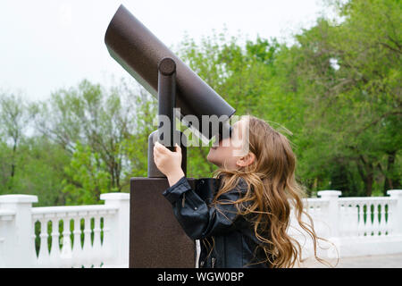 Modische kleines Schulmädchen, die durch stationäre Fernglas. Das Konzept von Lernen und neues Wissen. Close-up Stockfoto