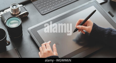 Nahaufnahme der weiblichen Designer Zeichnung auf Tablet in dunklen stilvolle Arbeitsplatz mit Kamera und Bürobedarf Stockfoto