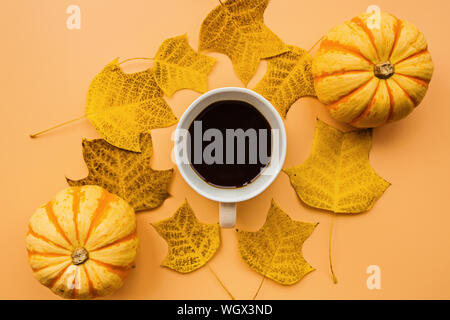 Herbst Rahmen aus Kürbissen, Tasse Kaffee und Laub auf orangem Hintergrund. Herbst, Halloween und Thanksgiving Konzept. Styled Lager flach Stockfoto