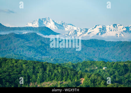 Grünen hügeligen Tal mit einsamen Haus und hohen schneebedeckten Berge am Horizont. Grüne Tal mit dörfliche Siedlungen im Licht des Sonnenuntergangs. Stockfoto