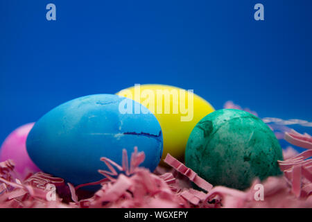 Blau, Rosa, Gelb, und Grün Ostereier auf rosa Ostern Gras mit einem blauen Hintergrund Stockfoto
