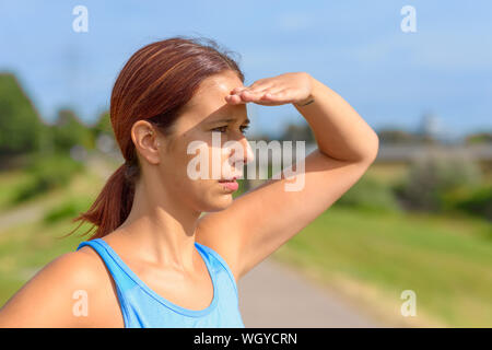 Attraktive gegerbt Frau, die gerade mit der Hand auf Ihre Augen und einem nachdenklichen ernste Ausdruck im freien im Sommer Sonnenschein Stockfoto