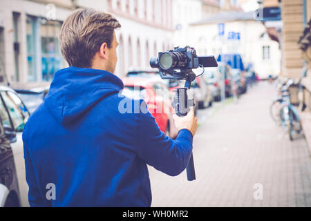 Stattliche Einflussnehmer Vlogger machen Video mit spiegellosen Kamera und Gimbal in der Stadt Stockfoto
