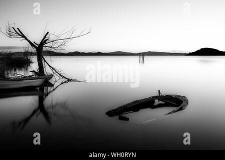 Eine fast vollständig versenkt kleines Boot in See Trasimeno (Umbrien, Italien) in der Abenddämmerung, in der Nähe von einem Skelett Baum Stockfoto