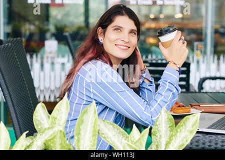 Portrait von Tagträumen lächelnden jungen Frau im Café draußen sitzen bei einer Tasse Kaffee in der Hand Stockfoto
