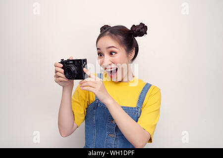 Überrascht, Frau, mit top knot Frisur, das Tragen von Jeans Overall, Holding retro Kamera, auf dem weißen Hintergrund Stockfoto