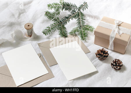 Weihnachten Tabelle, festlich gestaltete Komposition. Weihnachten Grußkarten und Umschläge Mock-ups. Handgefertigten Geschenkbox mit Seidenband, Tannenzapfen und Tannenbaum Stockfoto