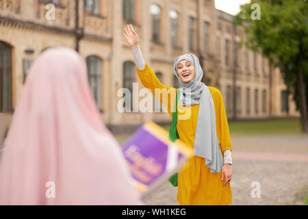 Muslimische Frau tragen gelbe Kleid ihr Freund winken Stockfoto