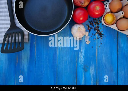 Frühstück. Pfanne, Tomaten, rohe Eier, Zwiebeln, Knoblauch, Gewürze. Selektive konzentrieren. Kopieren Sie Platz. Ansicht von oben. Auf blau Holz- Hintergrund. Close-up. Stockfoto