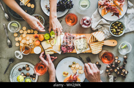 Mitte Sommer Picknick mit Wein und Snacks. Flachbild-lay von Wurst- und Käseplatte, Rose Wein, Nüsse, Oliven und Völker Hände über konkrete Tabelle backgr Stockfoto