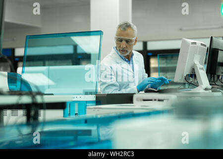 Aufmerksame grauhaarige männliche Person prüfen online Programm Stockfoto