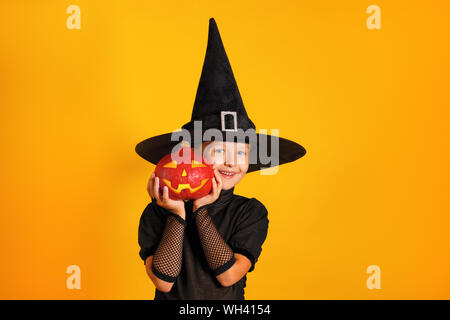 Süße kleine Mädchen in eine Hexe Kostüm hält einen Kürbis jack Lantern auf gelbem Hintergrund. Halloween Feier. Stockfoto