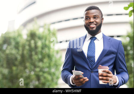 Gut aussehender Geschäftsmann stand draußen mit Kaffee und Smartphone in den Armen Stockfoto