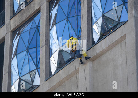 Scheibenwaschanlage in gelber Schutzkleidung gekleidet, Klettern auf ein modernes Gebäude. Stockfoto