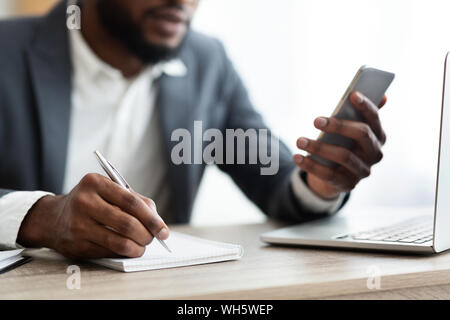 Afrikanische amerikanische Arbeitgeber mit Smartphone und Notizen im Büro Stockfoto