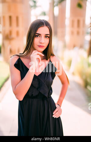 Junge lächelnde Frau in einem schwarzen Kleid zu Fuß entlang der Uferpromenade Stockfoto