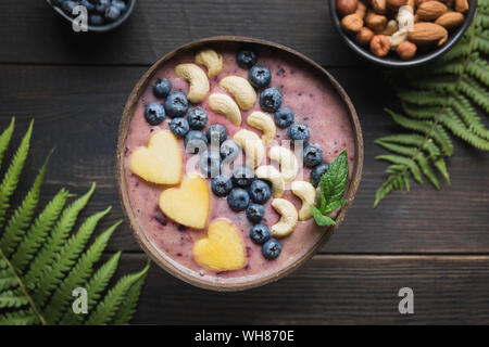 Gesunde tropisches Frühstück Banane und blueberry Smoothie mit Früchten in Coconut Schüssel auf holzbrett eingerichtet. Blick von oben. Sauber Essen, vegetar Stockfoto
