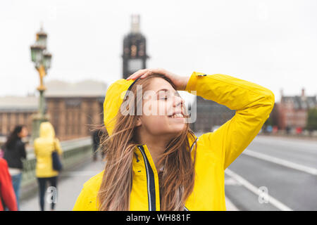 Glückliche junge Frau tragen gelbe Regenmantel an einem regnerischen Tag, London, UK Stockfoto