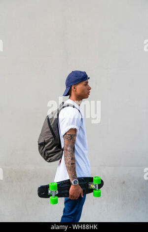 Tätowierten jungen Mann mit Skateboard und Rucksack vor grauem Hintergrund Stockfoto