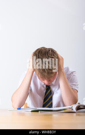 Ein gestresster Schüler mit dem Kopf in seinen Händen saß an seinem Schreibtisch Stockfoto