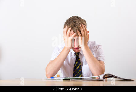 Ein gestresster Schüler mit dem Kopf in seinen Händen saß an seinem Schreibtisch Stockfoto