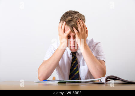 Ein gestresster Schüler mit dem Kopf in seinen Händen saß an seinem Schreibtisch Stockfoto