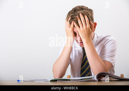 Ein gestresster Schüler mit dem Kopf in seinen Händen saß an seinem Schreibtisch Stockfoto