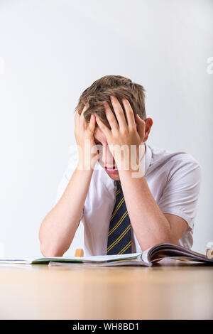 Ein gestresster Schüler mit dem Kopf in seinen Händen saß an seinem Schreibtisch Stockfoto