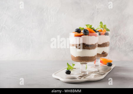 Aprikose Kleinigkeit, Schokolade, Biskuit, mehrschichtige Desserts mit frischen Beeren und sanften Frischkäse auf grauem Hintergrund. Horizontale Ansicht. Raum fo Text. Stockfoto