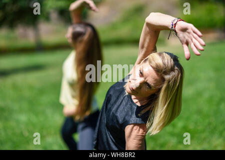 Reife frau yoga mit ihrer Tochter in einem Park Stockfoto
