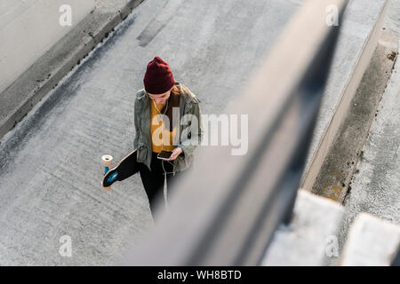 Stilvolle junge Frau mit Skateboard und Handy auf dem Parkdeck Stockfoto