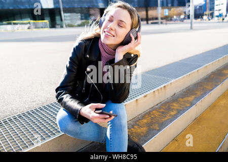 Porträt der jungen Frau hört Musik mit Smartphone und Kopfhörer, Barcelona, Spanien Stockfoto