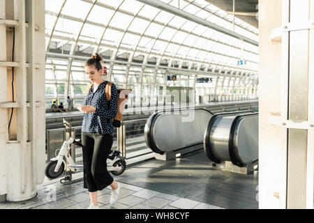 Junge Frau mit Elektroroller und Handy am Bahnhof Stockfoto